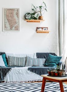 A cozy living room with large windows, indoor plants, a couch with pillows, a geometric rug, and wall shelves with decorations ends the sentence.