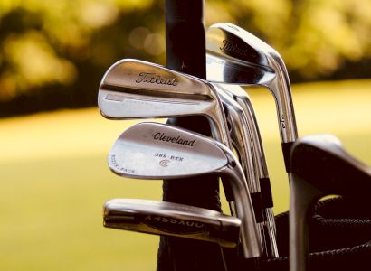The image shows a set of golf clubs with brands such as Titleist and Cleveland, placed in a golf bag with a grassy background.