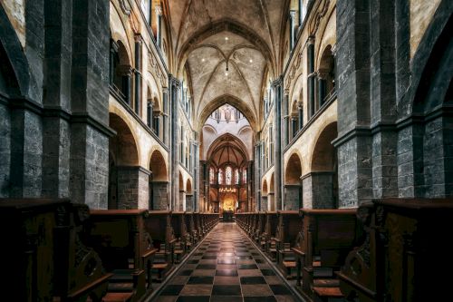 The image shows the interior of a grand cathedral with high arches, stained glass windows, and symmetrical aisle seating on either side.