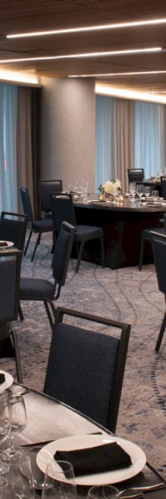 The image shows an elegantly set banquet hall with round tables and black chairs, decorated with flowers and candles, ready for an event.